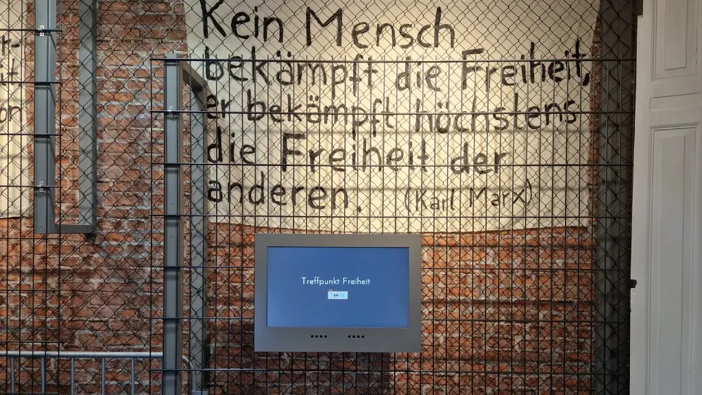 Treffpunkt Freiheit title screen on a wall of the exhibition, next to a chain-link fence with a Karl Marx quote about freedom